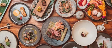 A variety of dishes on a wooden table, including sushi, sashimi, and other Asian cuisine.