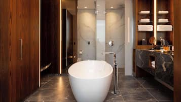 A modern bathroom with a freestanding bathtub, a vanity with a marble countertop, and a wooden vanity with shelves holding towels.