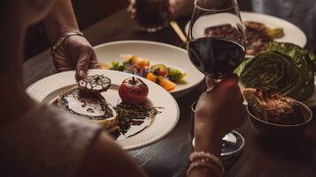 A dining table with plates of food, a bowl of bread, and glasses of red wine.