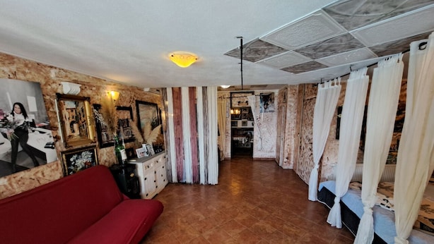 A room with a red sofa, a wooden floor, a ceiling with a light fixture, and a bed with white curtains. - Villa Georgina With Cats (Opatija)