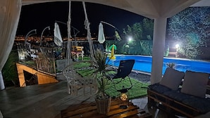 An outdoor patio with wooden furniture, a potted plant, and a pool in the background. - Villa Georgina With Cats (Opatija)