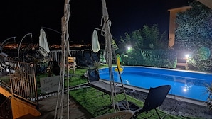 A nighttime pool area with lounge chairs, a swing chair, and a sign indicating the villa name. - Villa Georgina With Cats (Opatija)