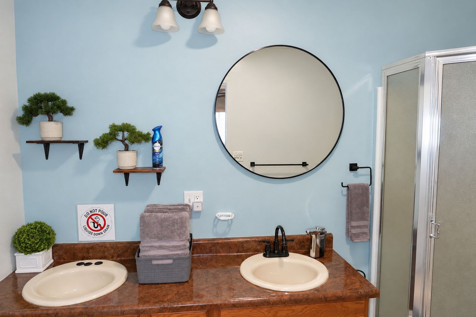 A bathroom with two sinks, a round mirror, a towel rack, and a shower door.