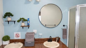 A bathroom with two sinks, a round mirror, a towel rack, and a shower door.