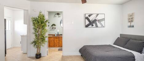 Une chambre à coucher avec un lit, un ventilateur de plafond, une plante en pot et des œuvres d’art accrochées aux murs.