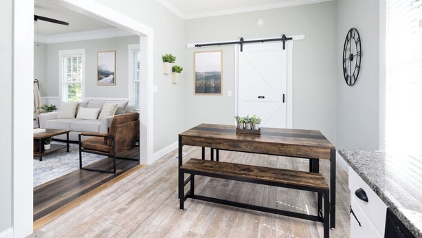 A modern kitchen with a wooden table, bench, and a clock on the wall.
