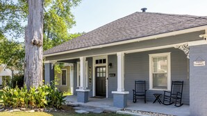 A single-story house with a porch, a large tree, and a small garden.