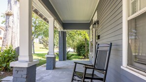 A covered porch with a bench and a chair, a window, and a view of a green landscape.