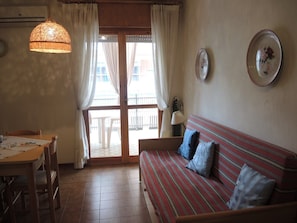Ein Zimmer mit einem Holztisch, einem gestreiften Sofa, einer Hängelampe und Blick durch eine Glastür.