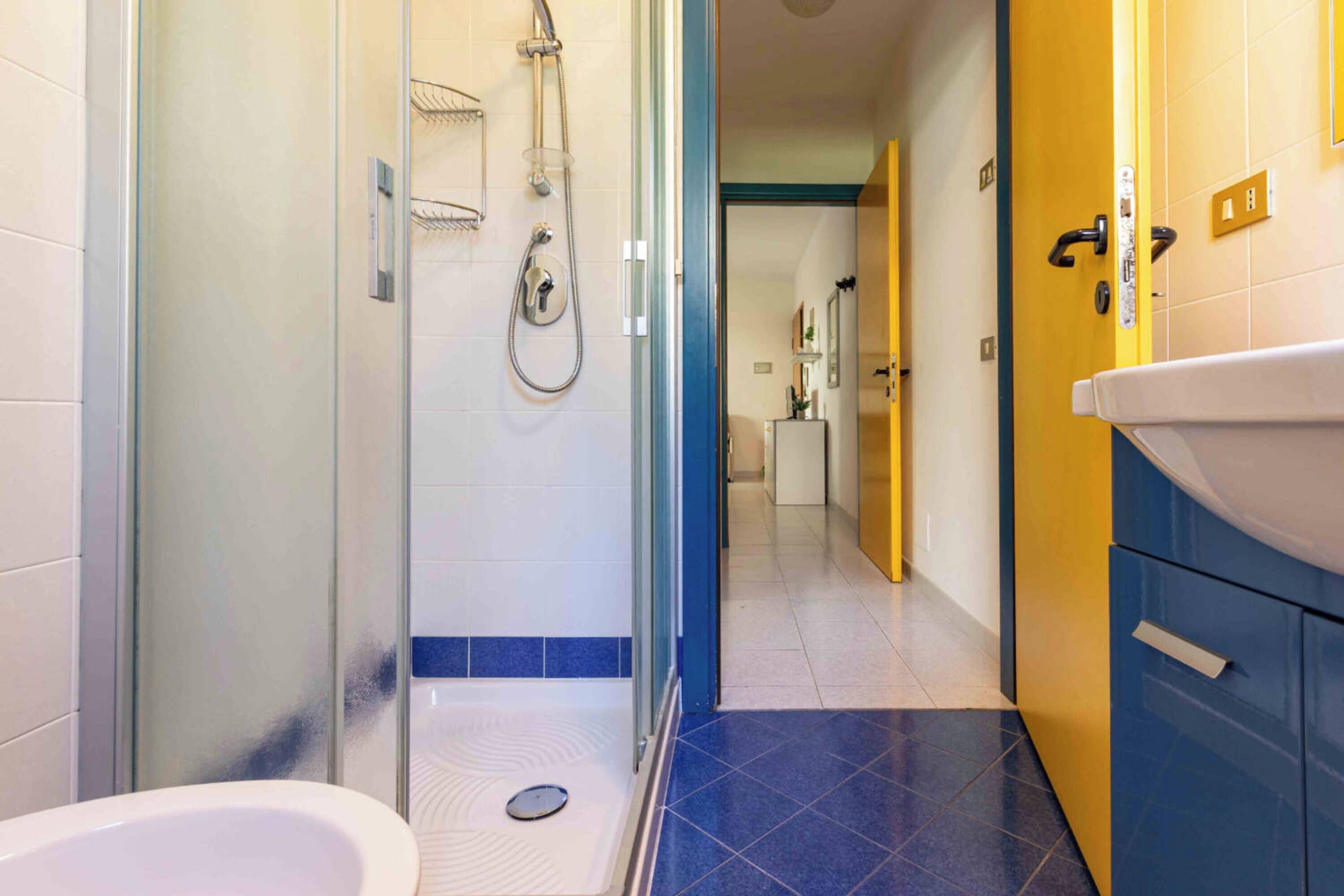 A modern bathroom with a glass shower enclosure, a white sink, and blue-tiled flooring.
