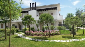 Ein modernes Gebäude mit weißer Fassade, mehreren Schornsteinen und einem Garten mit Bäumen und rosa Blüten.