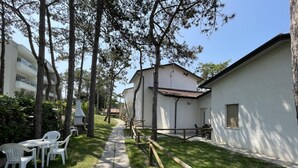 A pathway leading to a building with a white exterior, surrounded by trees and a grassy area with white plastic chairs. - Gorgeous Villa Close to the sea (San Michele al Tagliamento)