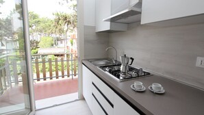 A modern kitchen with white cabinets, a gas stove, and a view of a balcony with a wooden fence. - Gorgeous Villa Close to the sea (San Michele al Tagliamento)