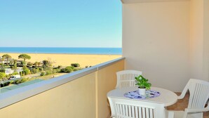 A balcony with a view of the beach, white chairs, a table with a potted plant, and a blue and white plate. - Nice Apartment With Terrace and Swimming Pool (San Michele al Tagliamento)