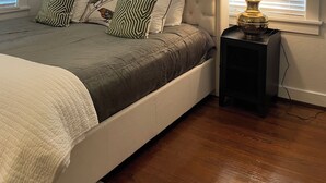 A bedroom with a tufted headboard, a bed with a quilted blanket, patterned pillows, a bedside lamp, and a ceiling fan. - Masters rental - Designer MCM updated bungalow   (Augusta)