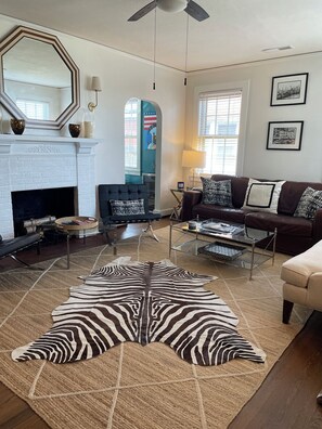 A living room with a fireplace, a sofa set, a zebra-patterned rug, and a large mirror.