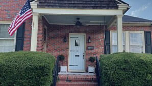 A brick house with a white front door, a small porch, and an American flag. - Masters rental - Designer MCM updated bungalow   (Augusta)