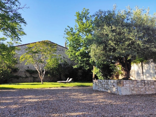 Un bâtiment en pierre doté d’un toit en pente, entouré d’une allée gravillonnée et d’une zone herbeuse.