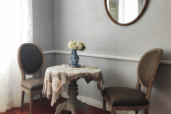 Una habitación con una mesa cubierta por un mantel de encaje, dos sillas, un jarrón con flores y un espejo en la pared.