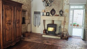 A room with a fireplace, wooden flooring, a large wooden cabinet, and a chandelier. - 4 Bed Villa - Sleeps 8 - Garden - Fireplace (Port-Sainte-Foy-et-Ponchapt)
