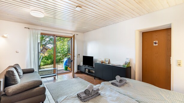 Et moderne hotelværelse med sofa, seng med håndklæder, fjernsyn og skydedør til terrassen.