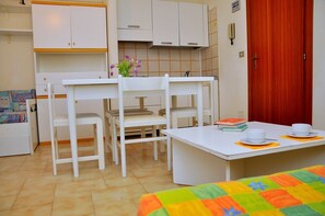 Una habitación pequeña y limpia con muebles blancos, una puerta roja y un salpicadero de azulejos.