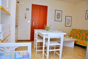 A small, well-lit room with a white table and chairs, a wooden door, and a colorful sofa. - Beautiful Studio Apartment in a Seafront Building (San Michele al Tagliamento)