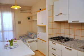 A compact kitchen with white cabinets, a gas stove, and a small dining area with a table and a chair. - Beautiful Studio Apartment in a Seafront Building (San Michele al Tagliamento)