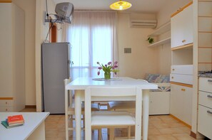 A compact kitchen with a white table, chairs, a refrigerator, and a window with curtains. - Beautiful Studio Apartment in a Seafront Building (San Michele al Tagliamento)