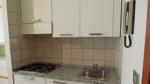 A compact kitchen with white cabinets, a granite countertop, a gas stove, and a sink. - Beautiful Studio Apartment in a Seafront Building (San Michele al Tagliamento)
