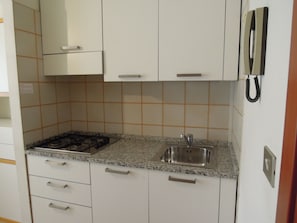 Une cuisine de taille réduite avec des meubles blancs, un plan de travail en granit, une cuisinière à gaz et un évier.