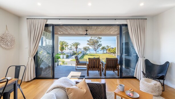 Un salon moderne comprenant un canapé, des fauteuils, une table basse et offrant une vue sur un jardin et la mer grâce à de grandes portes vitrées.