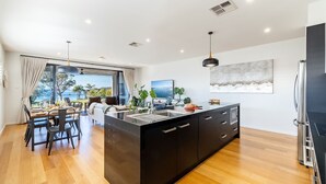 Une cuisine moderne dotée d’un îlot central, d’un coin repas offrant une vue agréable et d’une grande fenêtre donnant sur la mer.
