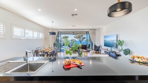Une cuisine moderne dotée d’un îlot central, un coin repas offrant une vue dégagée et un espace de vie avec une grande fenêtre donnant sur la mer.