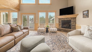 A spacious living room with a stone fireplace, leather sofas, and a flat-screen TV mounted above it. - Elk Ridge Retreat-25m to Yellowstone+hot tub+home theater (island park)
