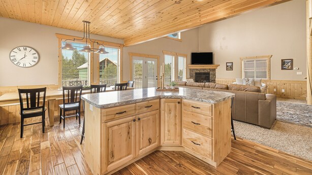 A spacious kitchen with wooden cabinets, a large island, and a dining area with chairs. - Elk Ridge Retreat-25m to Yellowstone+hot tub+home theater (island park)