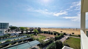 A view of a beach with a clear sky, a parking area with solar panels, and a building in the background. - Peaceful Seaside Flat With Pool in Bibione (San Michele al Tagliamento)