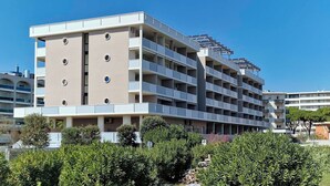 A multi-story building with balconies, solar panels on the roof, and a surrounding green area. - Peaceful Seaside Flat With Pool in Bibione (San Michele al Tagliamento)