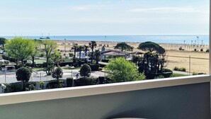 A view of a beachside area with a sandy beach, palm trees, and a few buildings in the background. - Peaceful Seaside Flat With Pool in Bibione (San Michele al Tagliamento)