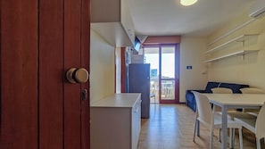 A compact kitchen with a refrigerator, a dining area with a table and chairs, and a sliding glass door leading to a balcony.