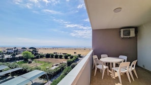 A balcony with a view of the beach and a table with chairs.