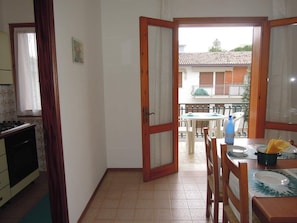 A kitchen with a stove, a dining area with a table and chairs, and a balcony with a view of a building. - Relaxing Villa With Private Garden Near the sea (San Michele al Tagliamento)