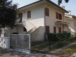 A two-story building with a staircase leading to the upper floor, a gated entrance, and a small garden area. - Relaxing Villa With Private Garden Near the sea (San Michele al Tagliamento)