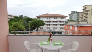 A balcony with a white table and two white chairs, overlooking a residential area with buildings and trees. - Comfortable Flat Next to the Beach-beahost (San Michele al Tagliamento)