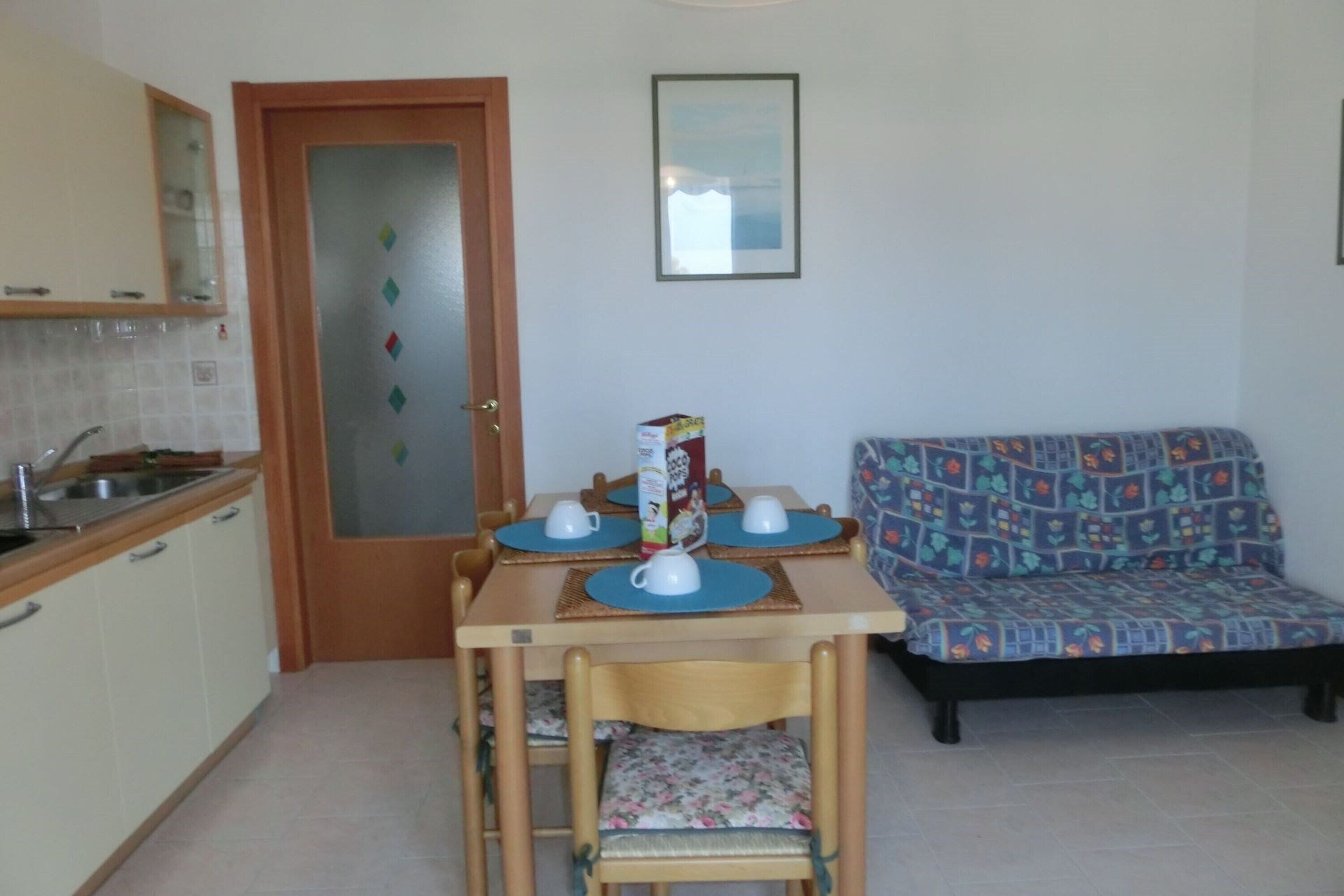 A small kitchen with a dining table set for two, a sofa, and a door with frosted glass panels.