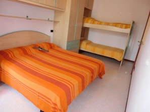 Une chambre comprenant un lit simple, un lit superposé, une armoire et une petite table avec une chaise.