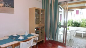 Un espace repas comprenant une table, des chaises, un buffet et donnant sur un espace extérieur aménagé grâce à une porte vitrée.