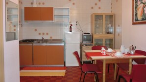 Une cuisine compacte avec un coin repas, comprenant une cuisinière, un évier, un réfrigérateur et un téléviseur posé sur un meuble.