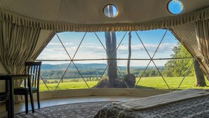 Een tent met uitzicht op een groen landschap, een bed, een stoel en een tafel.
