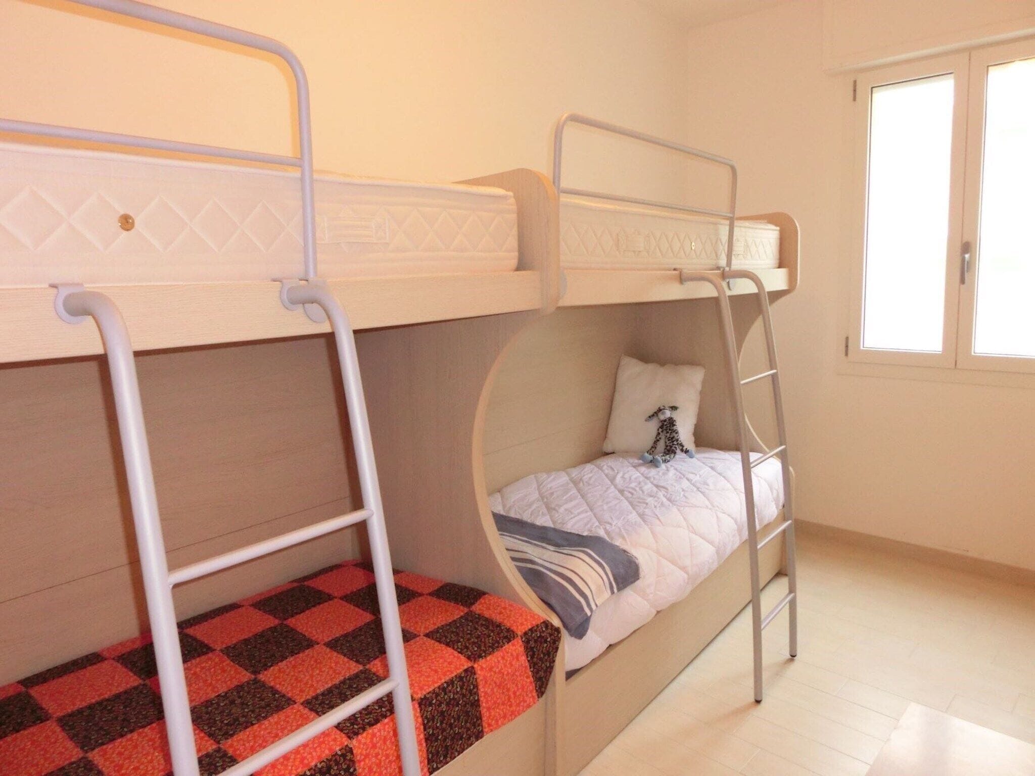 Une chambre avec un lit superposé, une fenêtre, un sol à carreaux et une échelle.